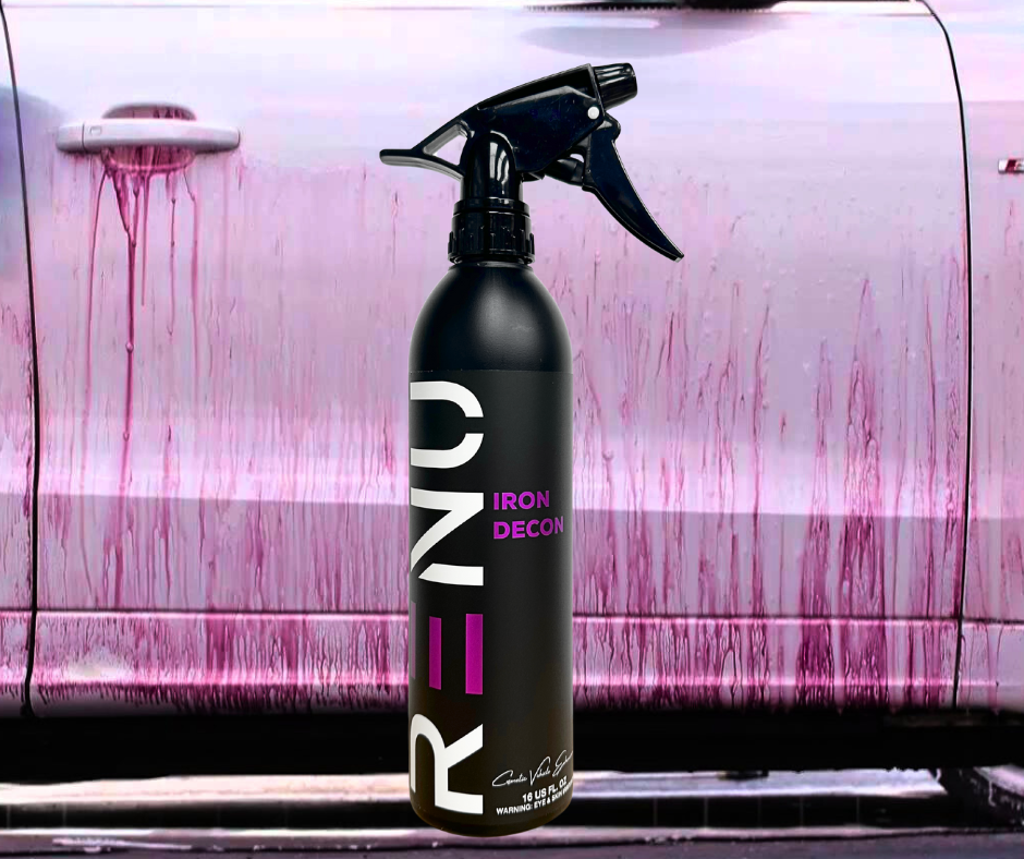 A black spray bottle labeled 'RENO IRON DECON' stands in front of a car door covered in pink and purple streaks of cleaning residue, suggesting a car interior or surface cleaner.