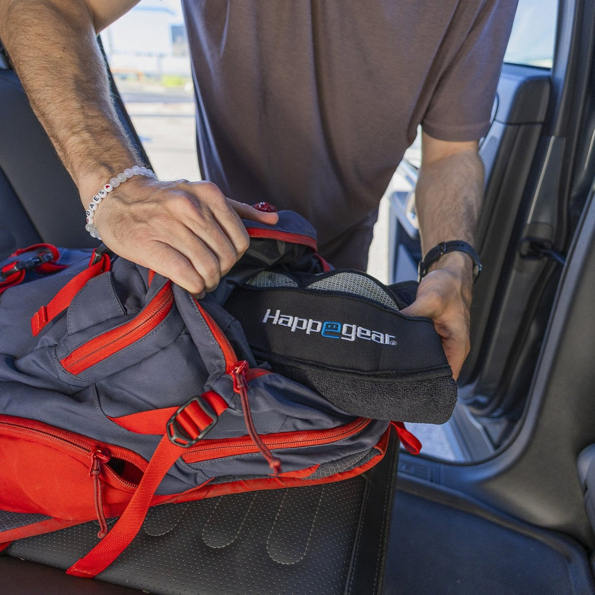 Person packing a Happegear Happeseat carry pouch into a backpack beside a car seat