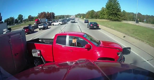 Image from dash cam footage of an accident where a red truck has been struck by a truck that pulls trailers.