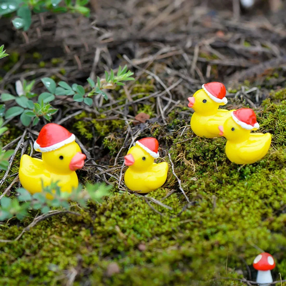 Four yellow rubber ducks wearing red Santa hats on a bed of green moss.