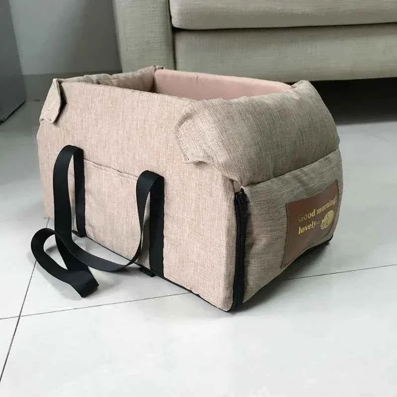 Beige pet carrier with black straps on a white floor.