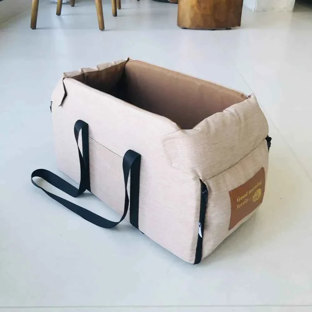 Beige pet carrier with black straps on a light gray floor