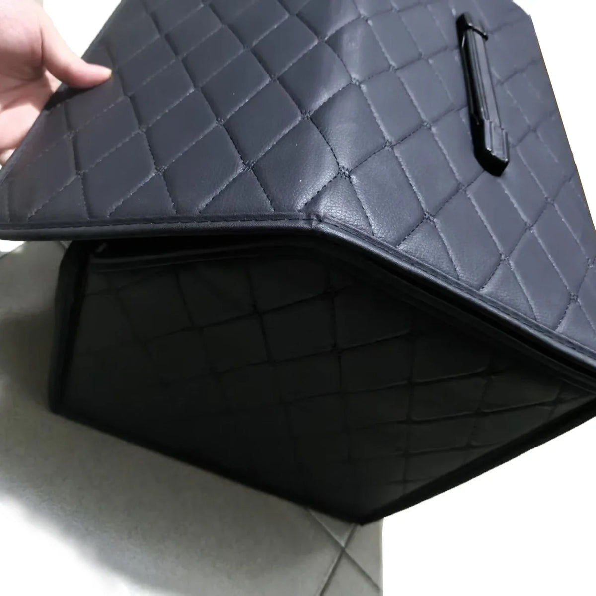 Black quilted car mat with a hand holding it, on a light gray surface.