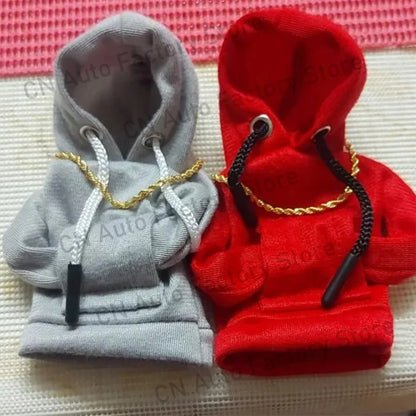Two small hoodies, one gray and one red, with gold chains on a textured surface.