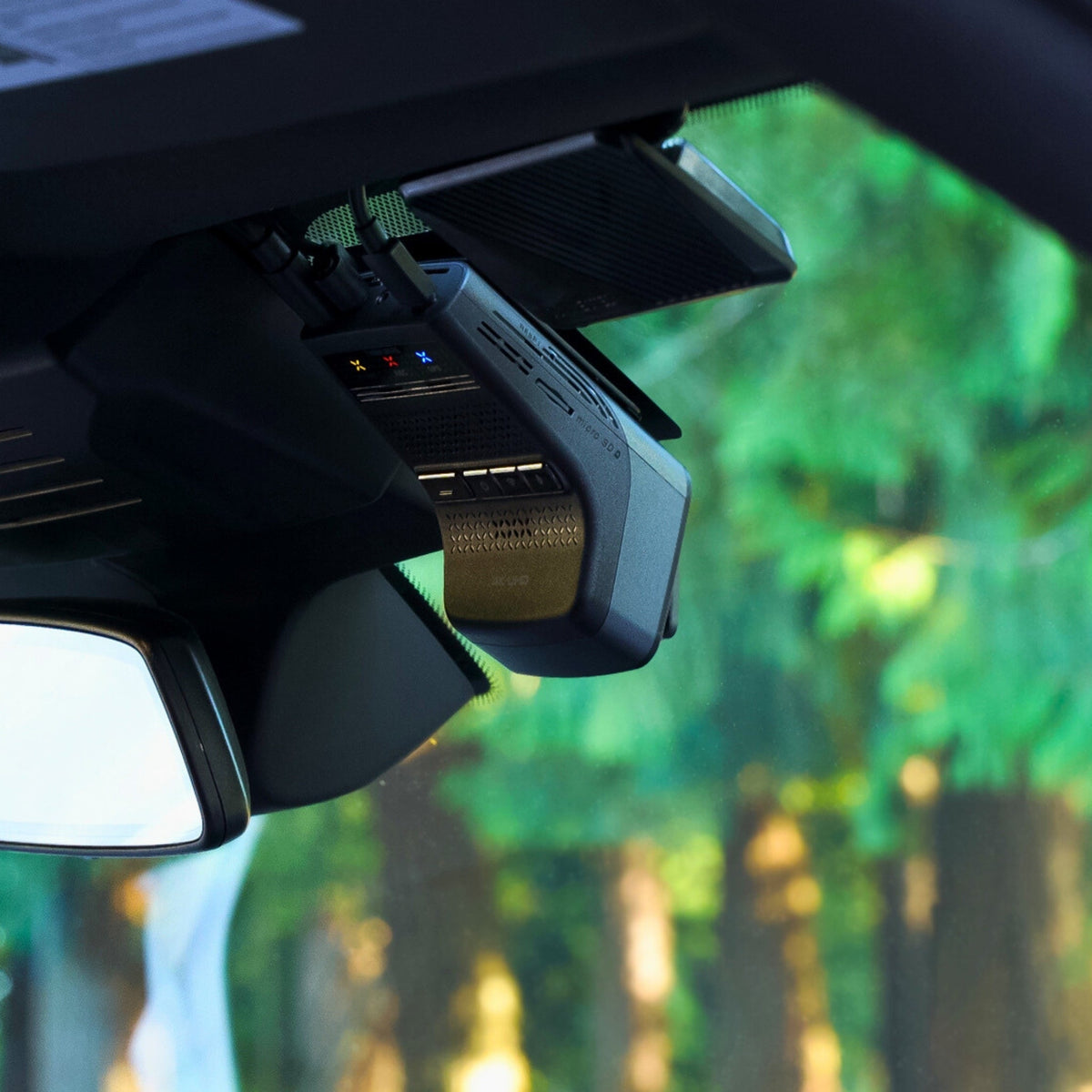 Car dashboard camera mounted on a car's interior ceiling with a blurred green outdoor background.